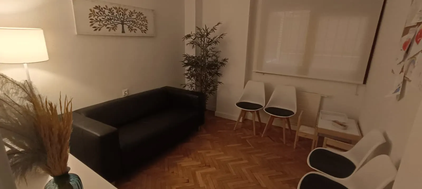 Sala de espera de BM Psicología: sofá, sillas, una mesa y una silla infantiles y dibujos de niños en la pared, con luz cálida.